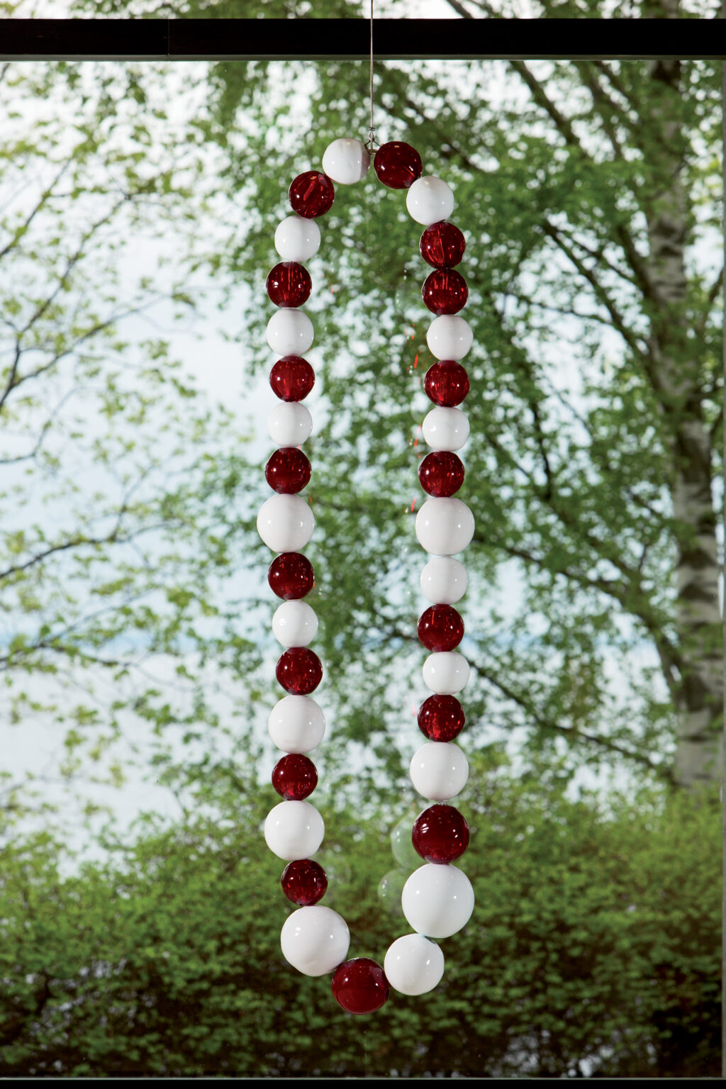 A giant white and red string of pearls in front of a window overlooking a lake.